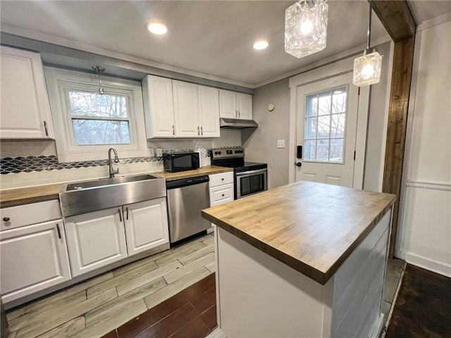 kitchen with a center island, stainless steel appliances, white cabinetry, and butcher block counters