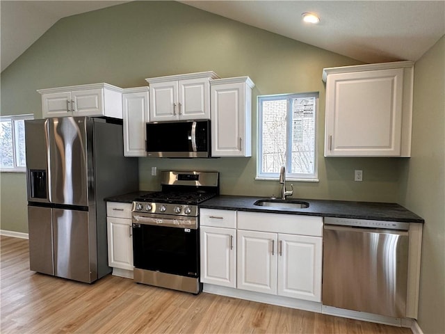 kitchen featuring sink, stainless steel appliances, lofted ceiling, white cabinets, and light wood-type flooring