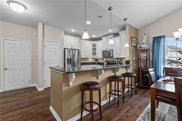 kitchen with kitchen peninsula, appliances with stainless steel finishes, decorative light fixtures, white cabinets, and dark hardwood / wood-style floors