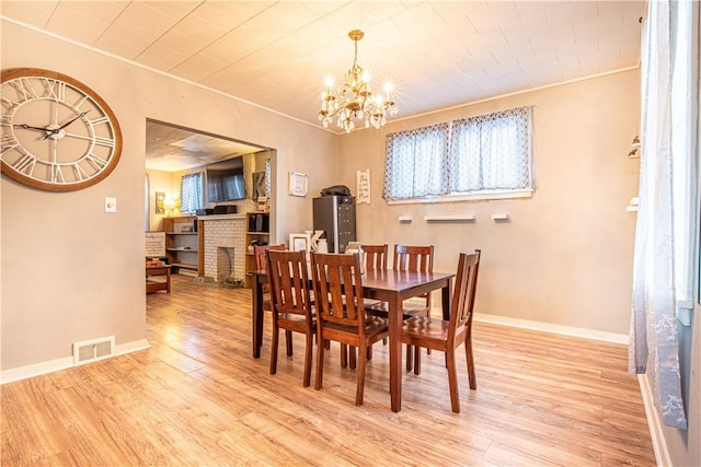 dining space featuring a fireplace, an inviting chandelier, and light wood-type flooring