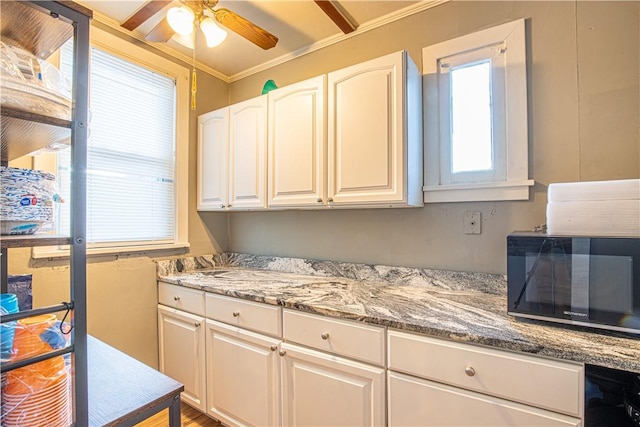 kitchen with white cabinetry, ceiling fan, ornamental molding, and light stone counters