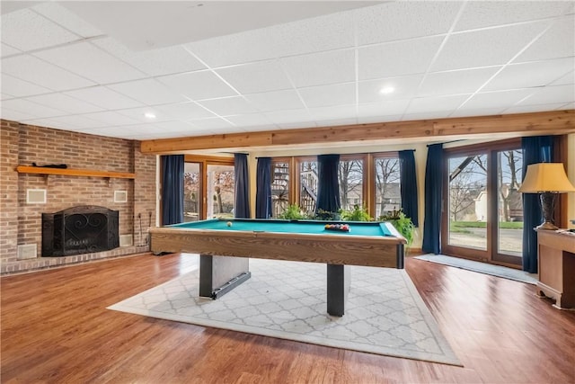 recreation room with hardwood / wood-style flooring, a drop ceiling, billiards, and a brick fireplace