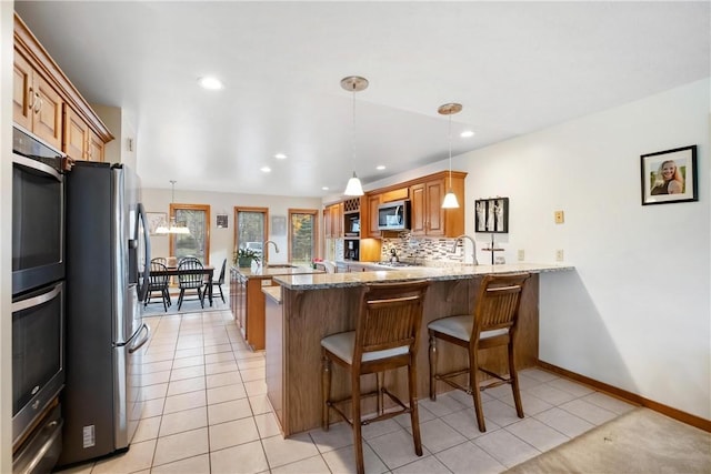 kitchen featuring tasteful backsplash, light stone counters, kitchen peninsula, light tile patterned floors, and appliances with stainless steel finishes