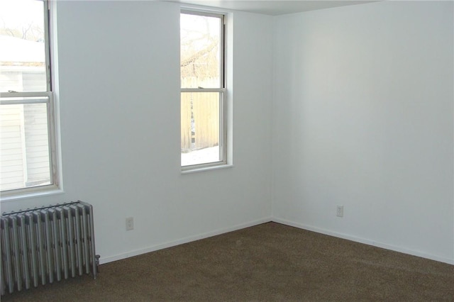 empty room featuring radiator, a healthy amount of sunlight, and dark carpet