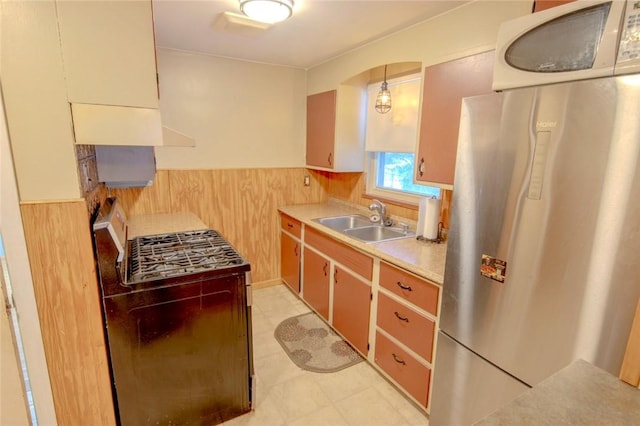 kitchen featuring stainless steel refrigerator, wood walls, sink, and decorative light fixtures