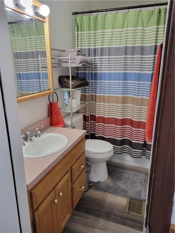 bathroom with hardwood / wood-style flooring, vanity, toilet, and walk in shower