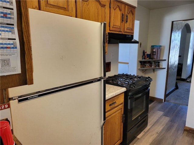 kitchen featuring black range with gas cooktop, dark hardwood / wood-style flooring, ventilation hood, and white fridge