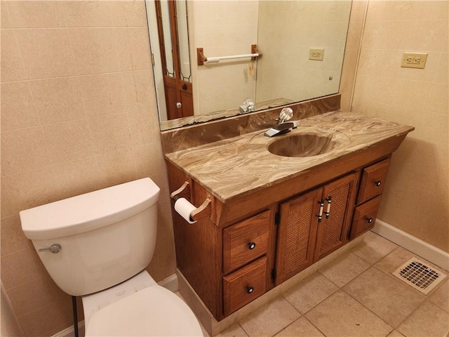 bathroom with toilet, vanity, tile patterned floors, and tile walls