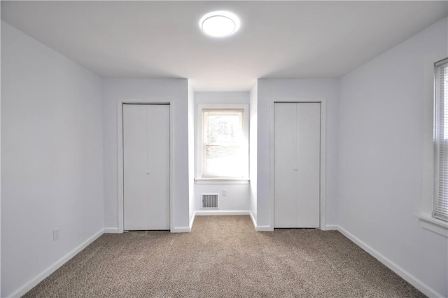 unfurnished bedroom with light colored carpet and multiple closets