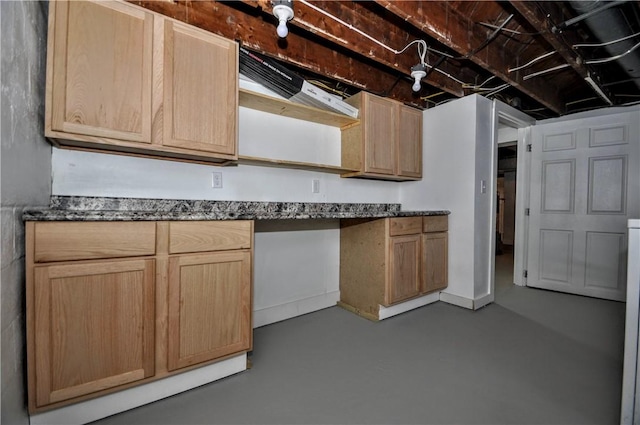 kitchen featuring light brown cabinets, dark stone countertops, built in desk, and concrete floors