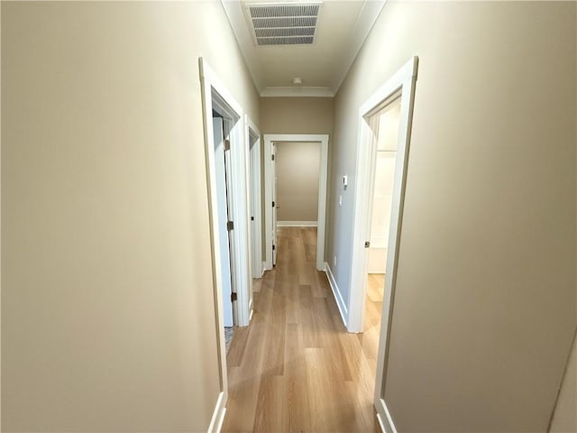 corridor featuring light wood finished floors, baseboards, visible vents, and crown molding