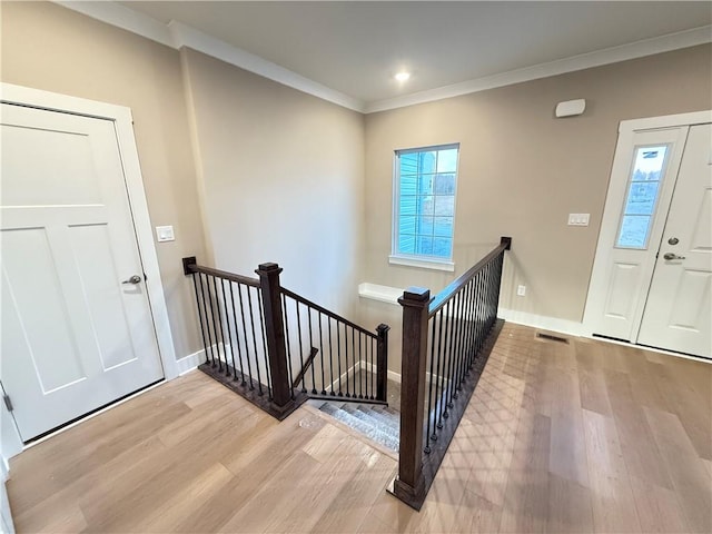 entryway with light wood-type flooring, visible vents, baseboards, and crown molding