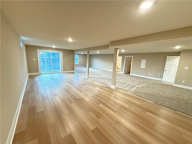 basement with visible vents, light wood-style flooring, and baseboards