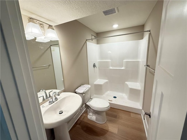 bathroom with visible vents, toilet, a stall shower, a textured ceiling, and wood finished floors