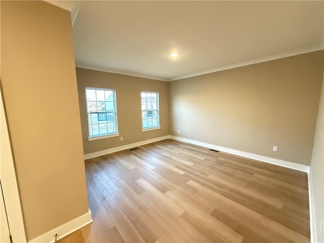 empty room featuring light wood-style floors, visible vents, baseboards, and crown molding