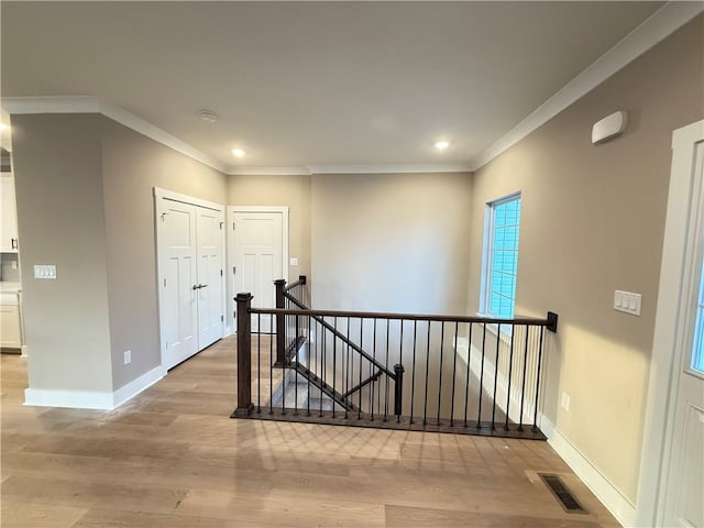 corridor featuring visible vents, crown molding, light wood-style flooring, and an upstairs landing