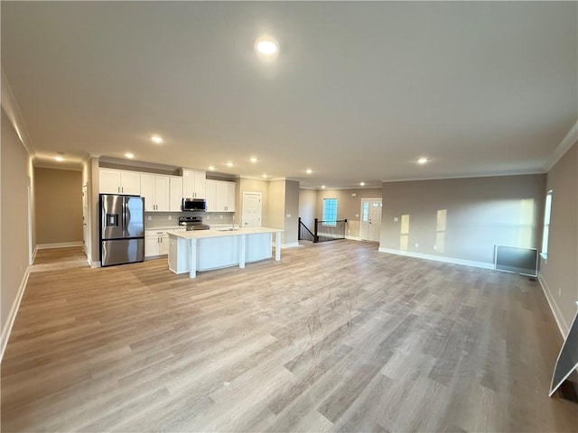 kitchen with a kitchen island with sink, stainless steel appliances, white cabinetry, open floor plan, and crown molding