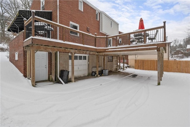 snow covered back of property with a wooden deck and a garage