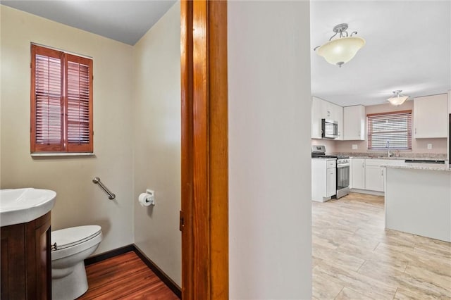 bathroom with baseboards, toilet, wood finished floors, and vanity