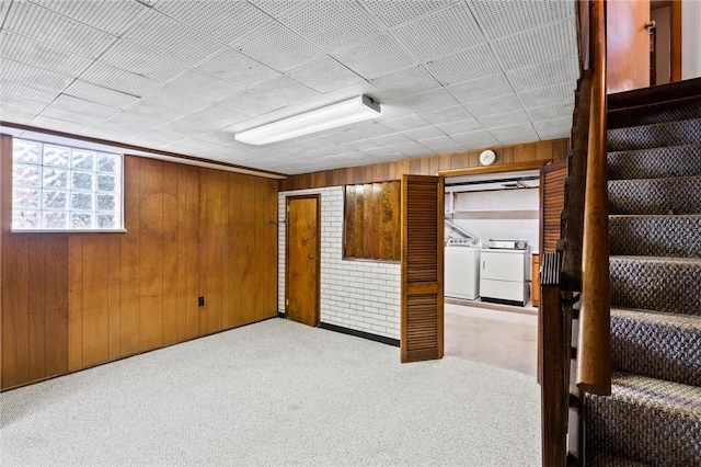 basement featuring washing machine and clothes dryer, wood walls, stairs, and carpet