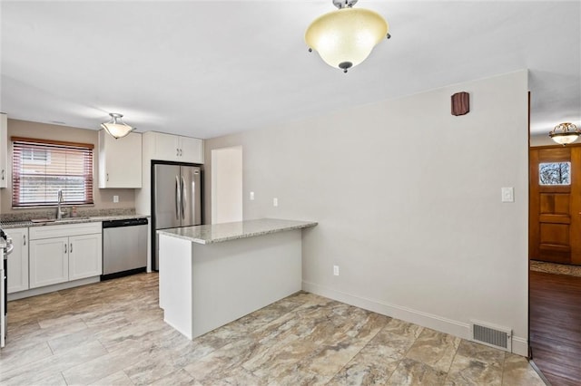 kitchen with light stone counters, appliances with stainless steel finishes, a peninsula, white cabinetry, and a sink