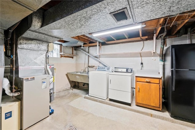 unfinished below grade area featuring heating unit, visible vents, separate washer and dryer, freestanding refrigerator, and a sink