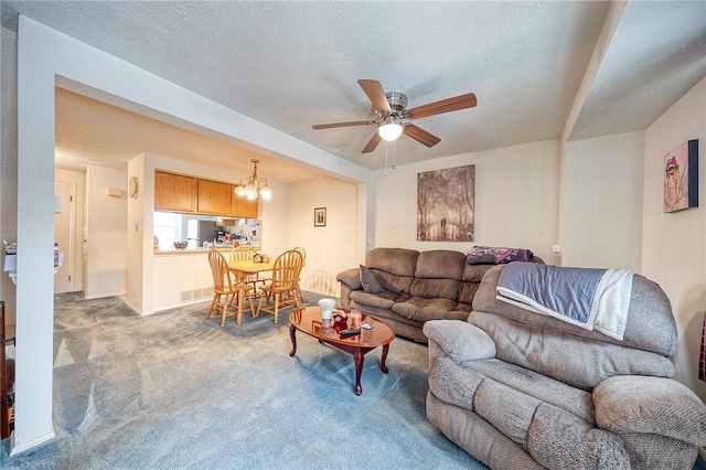 living room featuring ceiling fan with notable chandelier, light colored carpet, and a textured ceiling