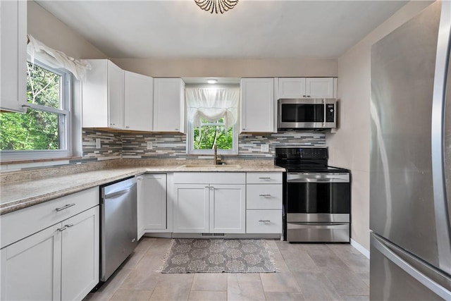 kitchen with light stone countertops, sink, backsplash, white cabinets, and appliances with stainless steel finishes