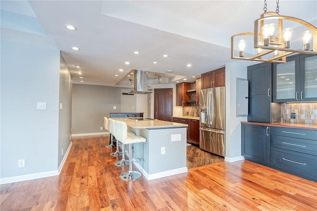 kitchen featuring a center island, a kitchen breakfast bar, stainless steel fridge with ice dispenser, pendant lighting, and island range hood