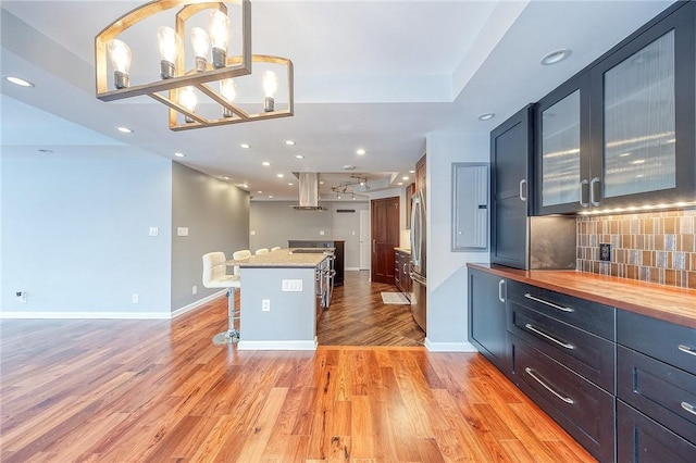 kitchen featuring a breakfast bar, light hardwood / wood-style flooring, range hood, tasteful backsplash, and decorative light fixtures