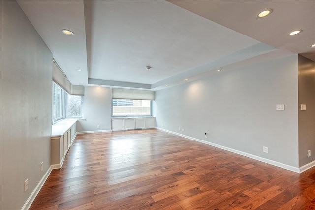 unfurnished living room featuring wood-type flooring, a tray ceiling, and a wealth of natural light