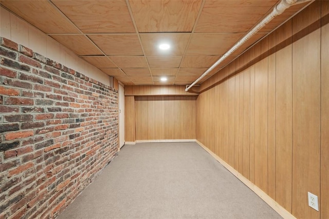 basement featuring carpet flooring, wood walls, wooden ceiling, and brick wall