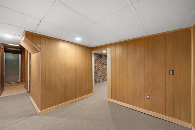 interior space with a drop ceiling, wood walls, light colored carpet, and brick wall