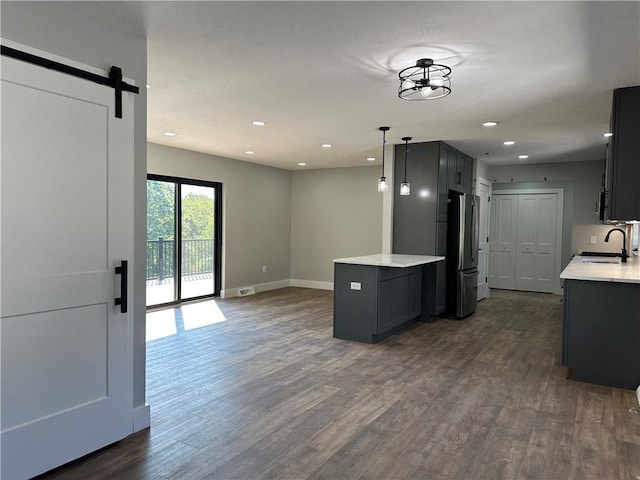 kitchen with sink, hanging light fixtures, stainless steel fridge, a barn door, and dark hardwood / wood-style flooring