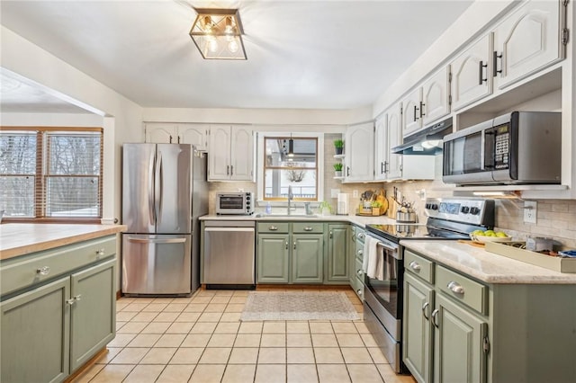 kitchen with stainless steel appliances, light tile patterned flooring, tasteful backsplash, and green cabinets