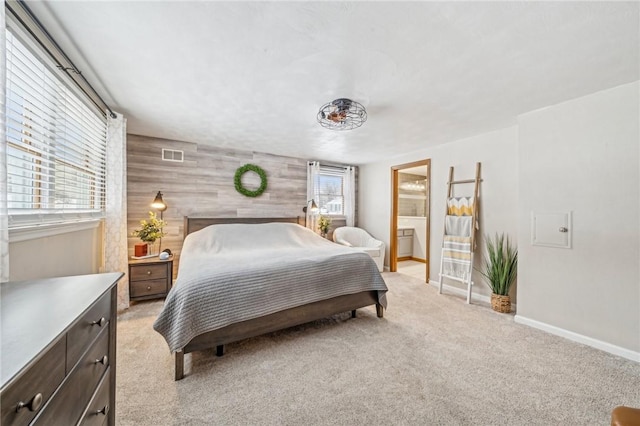 bedroom featuring wooden walls, ensuite bath, and light colored carpet