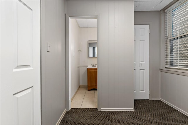 corridor with wood walls, light tile patterned floors, and sink