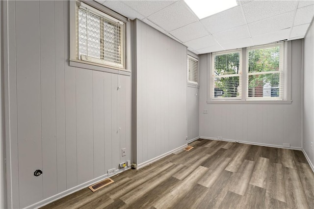 empty room with a paneled ceiling, wooden walls, and wood-type flooring