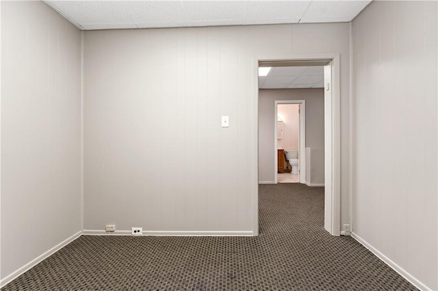 spare room with dark colored carpet and a paneled ceiling