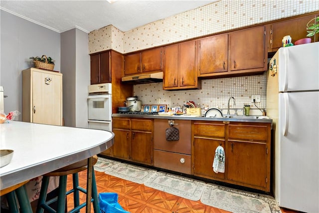 kitchen with white appliances, backsplash, ornamental molding, and sink