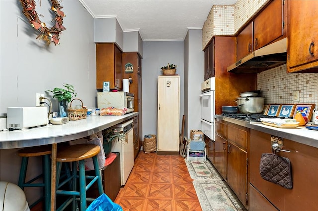 kitchen featuring a kitchen bar, backsplash, white oven, crown molding, and stainless steel gas stovetop