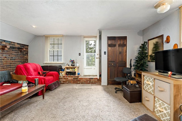 carpeted living room with a textured ceiling, brick wall, vaulted ceiling, and a brick fireplace