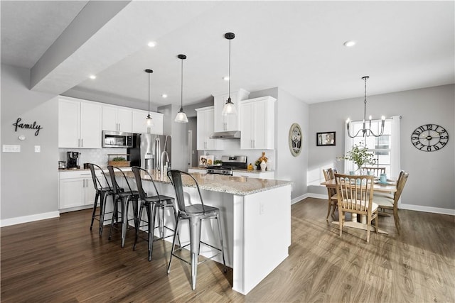 kitchen with stainless steel appliances, white cabinets, decorative light fixtures, a kitchen bar, and a center island with sink