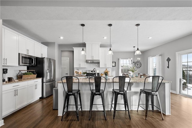 kitchen featuring stainless steel appliances, white cabinets, decorative backsplash, a center island with sink, and pendant lighting