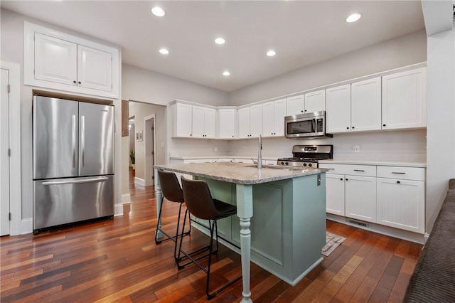 kitchen with a breakfast bar, white cabinets, dark hardwood / wood-style floors, an island with sink, and stainless steel appliances