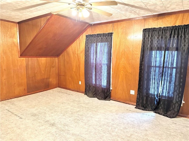 additional living space with light colored carpet, vaulted ceiling, ceiling fan, and wood walls