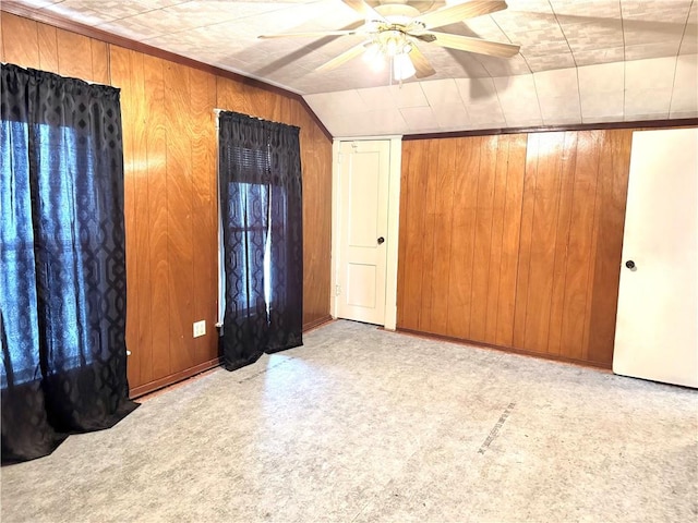 unfurnished bedroom featuring light colored carpet, vaulted ceiling, ceiling fan, and wood walls