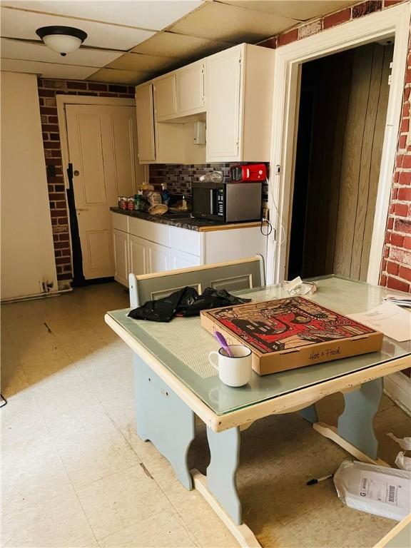 kitchen featuring white cabinets, a paneled ceiling, and brick wall