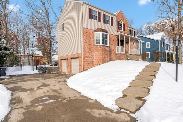 view of snowy exterior with a playground, covered porch, and a garage