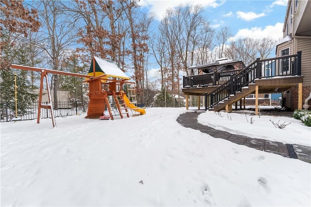 snowy yard featuring a playground and a deck